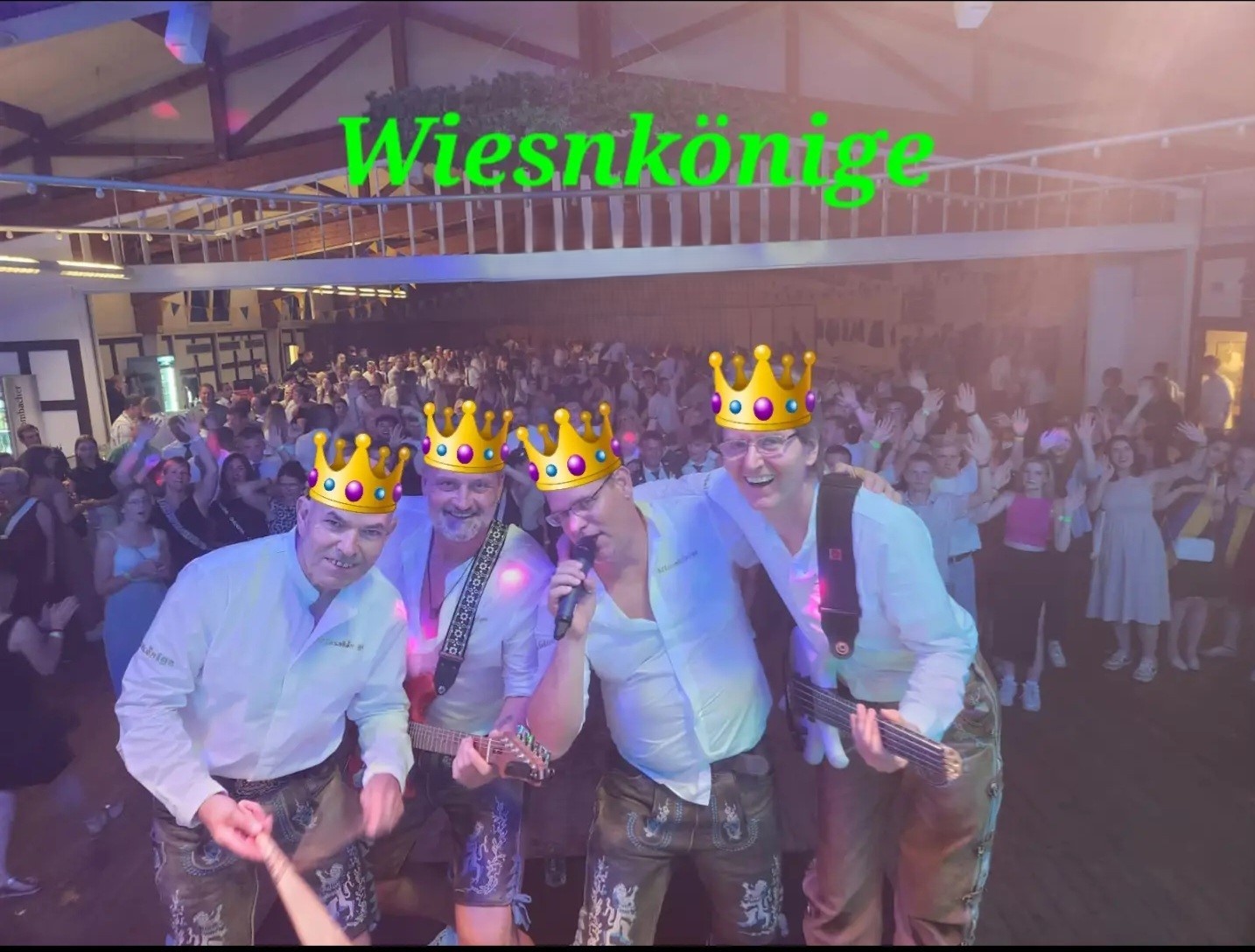 Die Wiesnkönige mit eingeblendeten Kronen auf der Bühne vor einem vollen Saal
