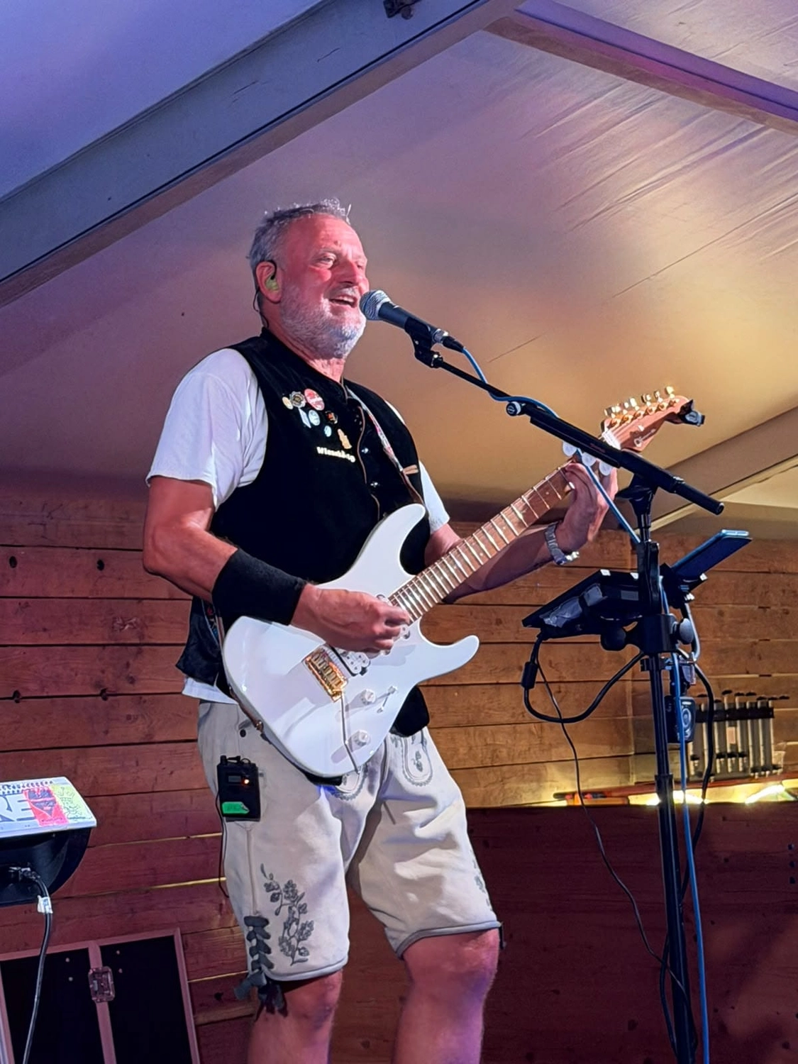Michael Stern mit weißer E-Gitarre am Mikrofon auf einer Holzbühne