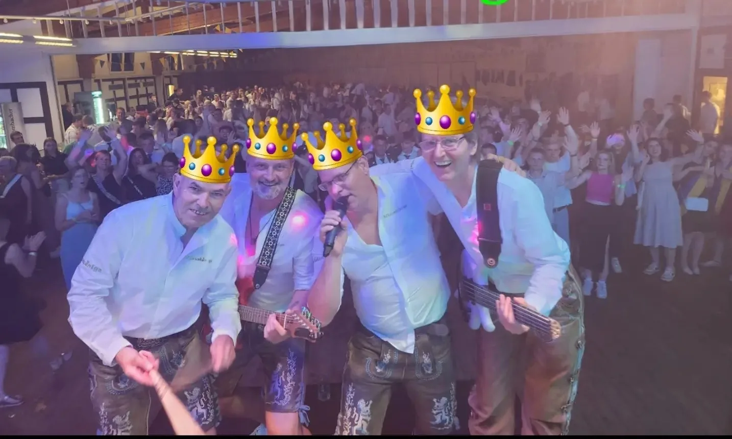 Vier Musiker der Wiesnkönige mit Kronen-Grafik auf der Bühne vor vollem Saal